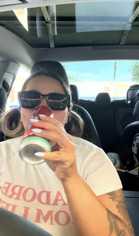 Mom in sunglasses sipping an iced drink in the car with her son's car seat in the back