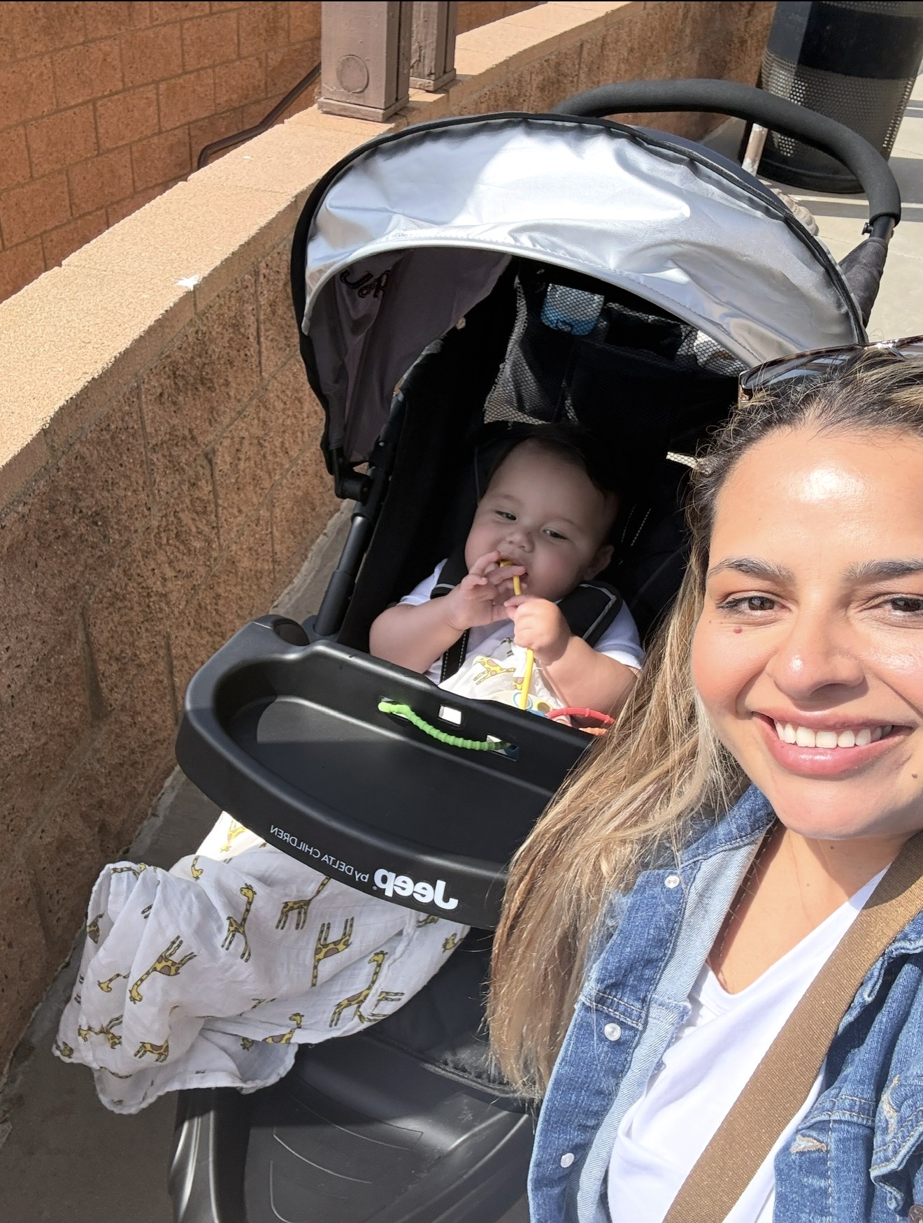 mother smiling with her baby boy in his keep stroller wrapped in muslin swaddle