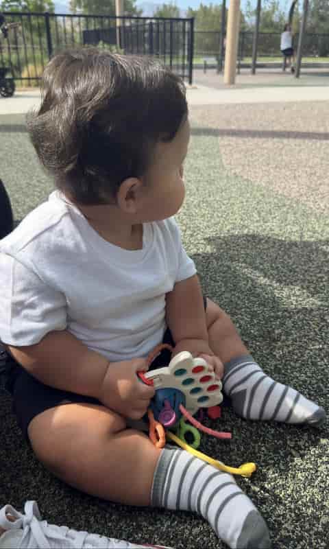 One-year-old boy sitting at the playground holding a colorful sensory toy