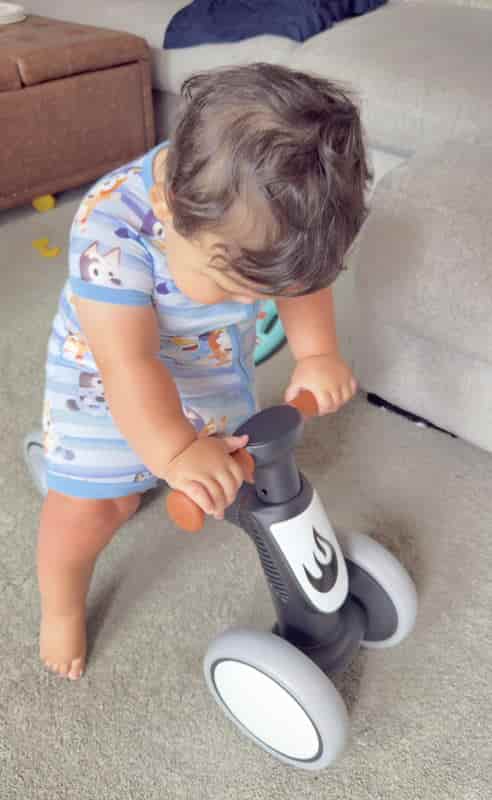 One-year-old boy standing at a mini balance bike on the living room floor