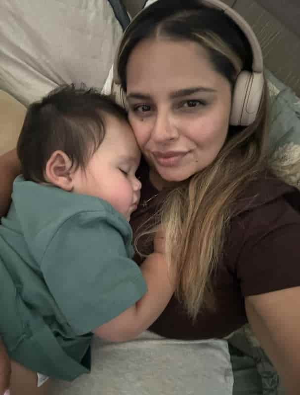 Exhausted mom wearing headphones cradling her sleeping one-year-old son